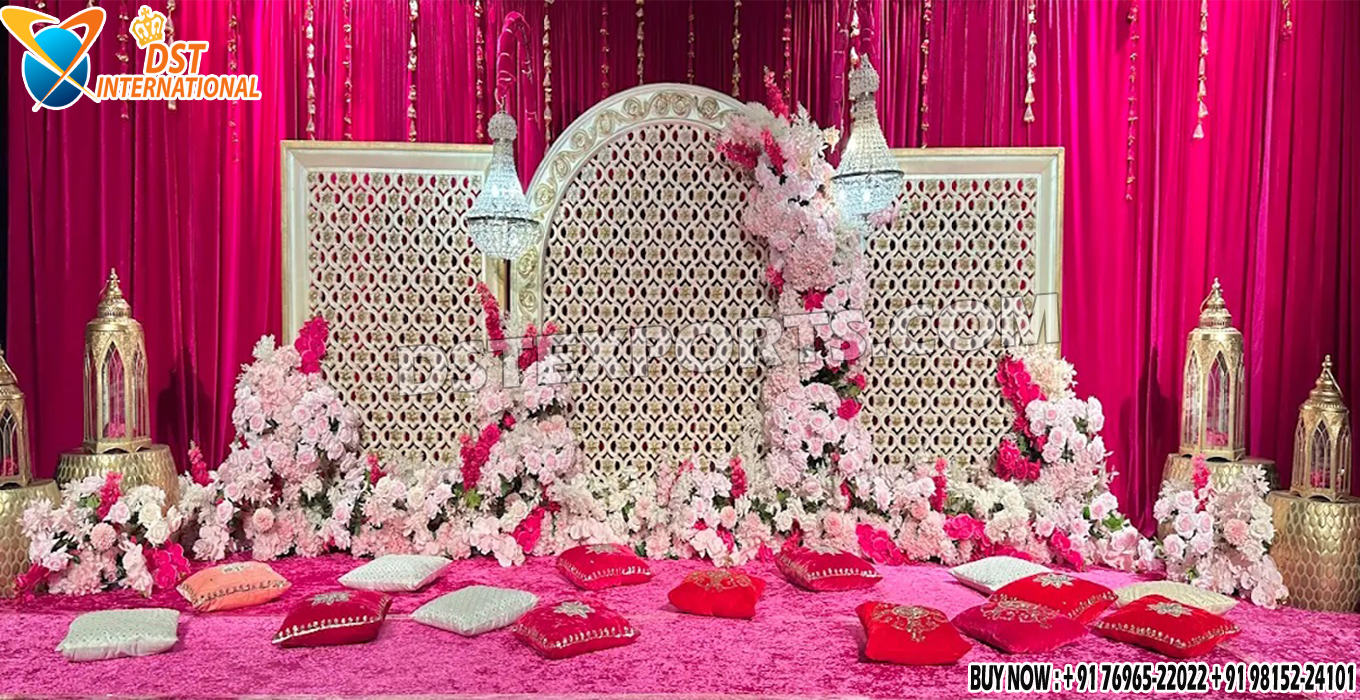 Grand Sangeet Ceremony Stage Setup in the UK featuring floral-decorated laser-cut panels, chandeliers, golden lanterns, pink velvet carpet, and embroidered cushions for a luxurious Indian wedding backdrop.