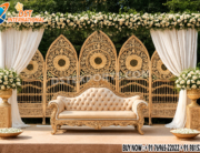 “Trending Designer Wedding Stage with golden carved metal backdrop frames, luxury sofa, white floral decorations, and elegant drapes – perfect for wedding and reception décor.”