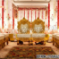 “Designer golden finish wooden mandap chairs set with heart-shaped backs, ivory cushions, and intricate carvings, placed on a beautifully decorated wedding stage with floral garlands and gold drapery.”