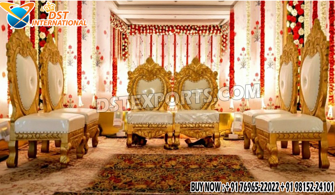 “Designer golden finish wooden mandap chairs set with heart-shaped backs, ivory cushions, and intricate carvings, placed on a beautifully decorated wedding stage with floral garlands and gold drapery.”