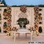 Elegant white laser-cut floral backdrop with pastel flower decorations and a single royal beige sofa, perfect for a luxury wedding reception stage setup in the USA.