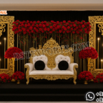 Royal golden fiber backdrop frames with ornate floral carving and luxury wedding reception stage setup with red floral arrangements and throne sofa.