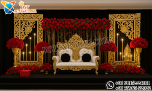 Royal golden fiber backdrop frames with ornate floral carving and luxury wedding reception stage setup with red floral arrangements and throne sofa.